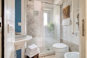 A bathroom with a glass shower enclosure, a white toilet, and a sink with a blue-tiled backsplash. - Bright 1BR with Balcony in Navigli (Milano)