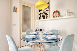 A dining area with a round glass table, blue chairs, and a yellow pendant light. - Bright 1BR with Balcony in Navigli (Milano)