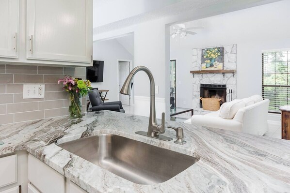 A modern kitchen with a large sink, marble countertops, and a dining area with a white sofa.