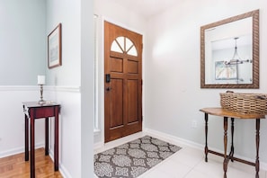 A hallway with a wooden door, a small table with a lamp, a rug, and a framed picture on the wall.
