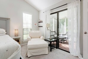 A bedroom with a bed, a chair, a table, and a view of an outdoor patio.