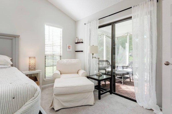 A bedroom with a bed, a chair, a table, and a view of an outdoor patio.