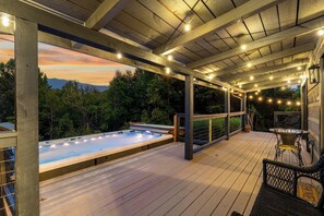 Eine Holzterrasse mit Whirlpool, Lichterketten und Blick auf die Berge.