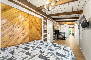 Ein Schlafzimmer mit Holzwand, einem Bett mit gemustertem Überwurf, einem an der Wand befestigten Fernseher und einem Flur, der in einen anderen Raum führt.