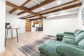 Ein moderner Wohnraum mit Holzboden, einem grünen Sofa, einem Couchtisch und einer Küchenzeile im Hintergrund.