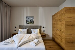 A modern hotel room with a large bed, a headboard, two bedside tables, a wooden wardrobe, and a framed picture on the wall. - 8002 Alpin Retreat Grand 2 (Schröcken)