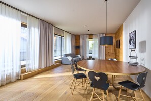 A modern dining area with a round wooden table, black chairs with heart cutouts, and a hanging light fixture. - 8002 Alpin Retreat Grand 2 (Schröcken)