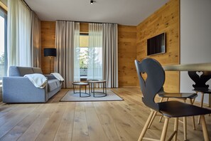Un salon moderne comprenant un canapé, deux petites tables, un fauteuil et un téléviseur fixé à un mur en bois.
