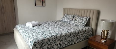 A bedroom with a bed, a nightstand, a lamp, a wardrobe, and a framed picture on the wall.