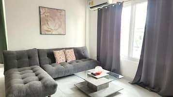 Una sala moderna con un sofá seccional gris, una mesa de centro de vidrio y un aire acondicionado instalado en la pared.