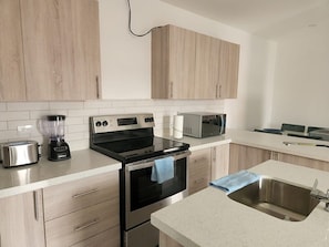A modern kitchen with stainless steel appliances, wooden cabinets, and a white countertop.