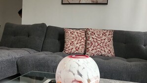 A living room with a grey sofa, a patterned throw pillow, a glass coffee table, and a vase with a marbled design.