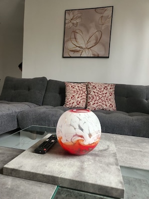A living room with a grey sofa, a patterned throw pillow, a glass coffee table, and a vase with a marbled design.