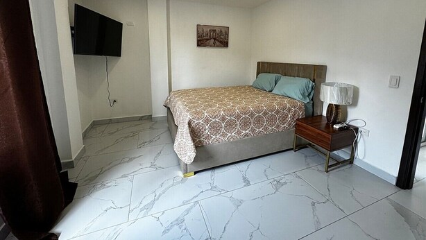 A bedroom with a bed, bedside table, lamp, and a mounted TV.