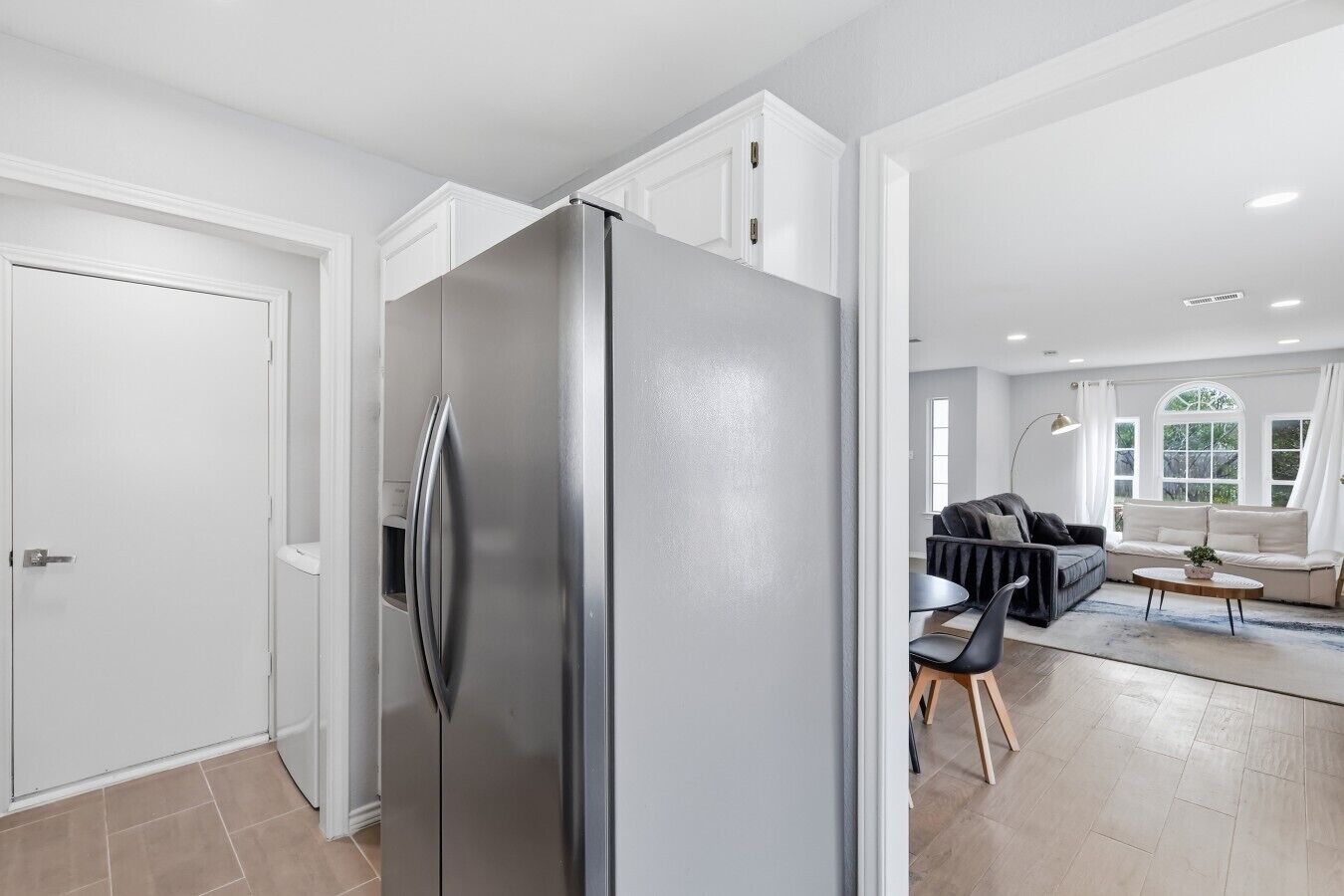 Una cocina moderna con un refrigerador de acero inoxidable, un comedor con un sofá y sillas, y un ventanal que proporciona luz natural.
