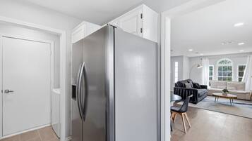 Una cocina moderna con un refrigerador de acero inoxidable, un comedor con un sofá y sillas, y un ventanal que proporciona luz natural.