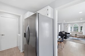 Eine moderne Küche mit einem Edelstahl-Kühlschrank, einem Essbereich mit einer Couch und Stühlen sowie einem großen Fenster, das für natürliches Licht sorgt.