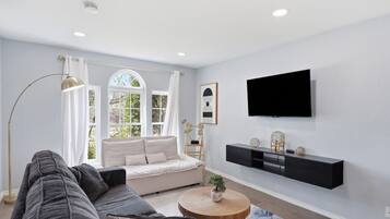 A modern living room with a sofa, a coffee table, a floor lamp, a TV, and a window with curtains.