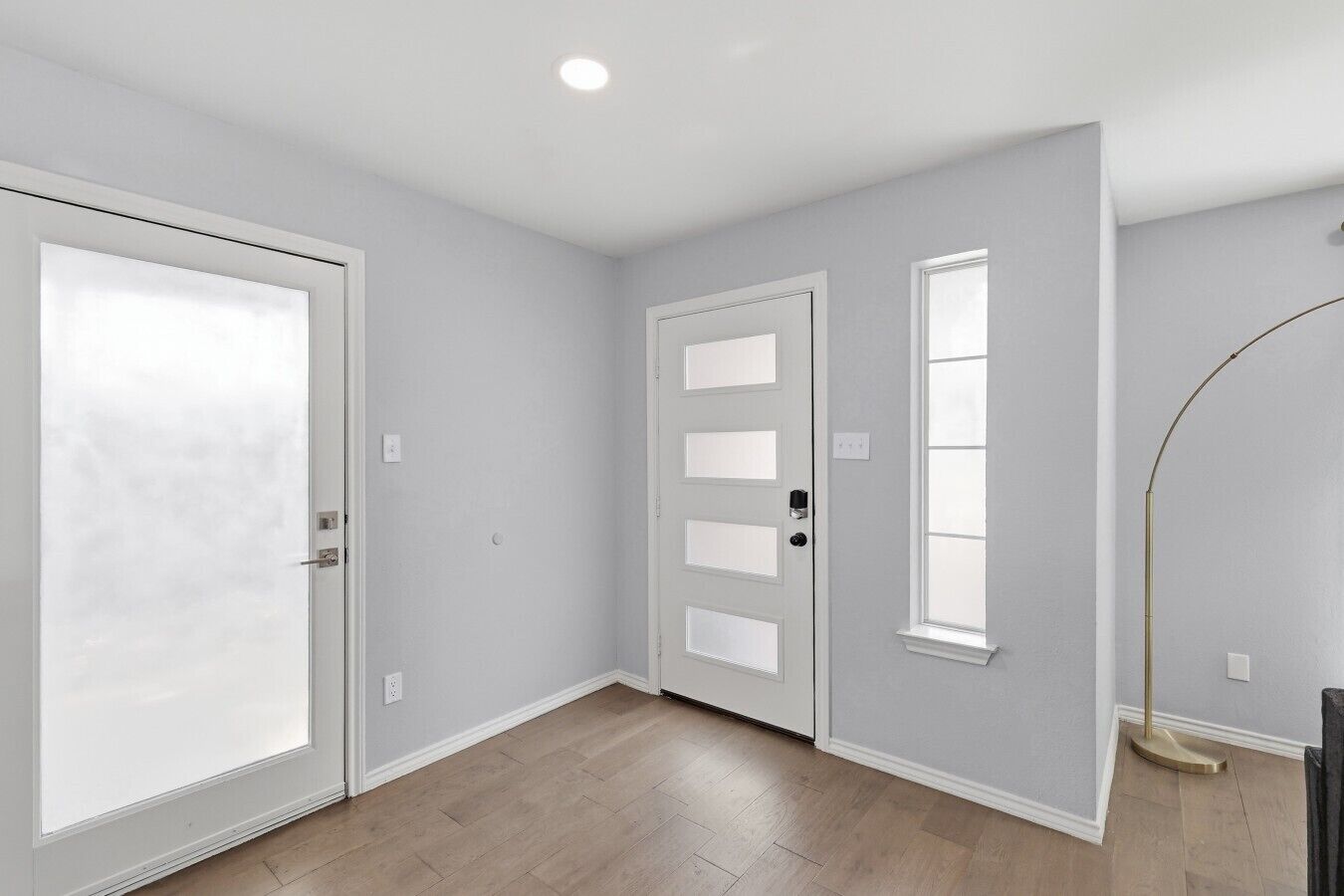 Una habitación con una puerta grande de color blanco, una puerta más pequeña con ventana y una lámpara de pie.