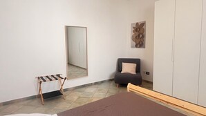 Ein Schlafzimmer mit Bett, Stuhl, Kleiderschrank, Spiegel und einer kleinen Bank.