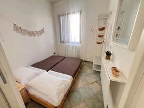 Une petite chambre à coucher, bien rangée, avec un lit, une table de chevet, un miroir et une fenêtre avec des rideaux.