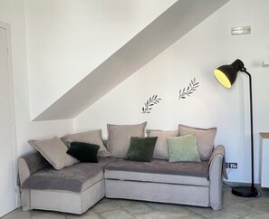Un coin salon avec un canapé d’angle gris, un lampadaire noir et des autocollants décoratifs en forme de feuilles fixés au mur.