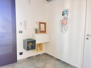 A hallway with a door, a wall-mounted phone, a framed certificate, a small shelf with a bowl and flowers, and a wall art piece. - Casa Nicolas 158 - Salento Explorer (Neviano)