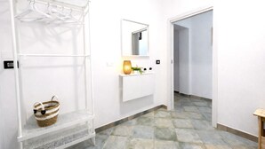 Ein Flur mit weißer Wand, einem Kleiderständer, einem Korb, einem Spiegel und einem Regal mit Pflanzen.