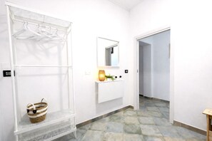 A hallway with a white wall, a hanging rack with clothes, a basket, a mirror, and a shelf with plants. - Casa Nicolas 158 - Salento Explorer (Neviano)