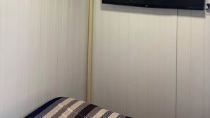 A room with a mounted television on the wall, an air conditioning unit above, and a bed with striped bedding.