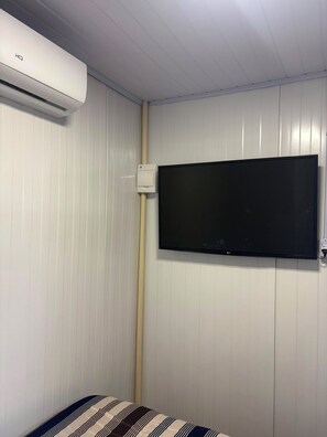 A room with a mounted television on the wall, an air conditioning unit above, and a bed with striped bedding. - New studio apartment with air conditioning, Wi-Fi, and parking. (Joinville)