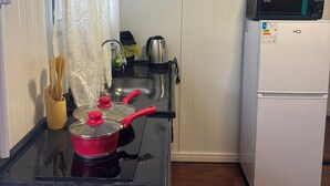 A compact kitchen with a stove, a kettle, a microwave, and a refrigerator.