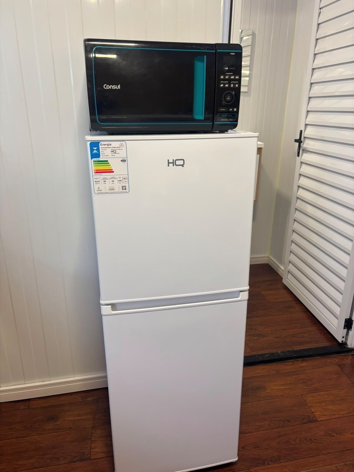 A white refrigerator with a black microwave on top, labeled 'HQ' and 'Consul.'