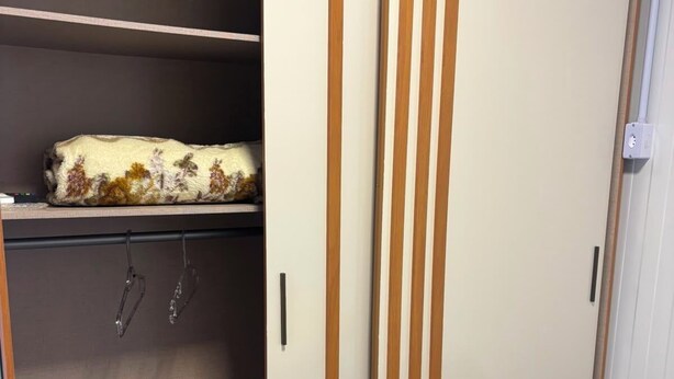 A wardrobe with a sliding door, a shelf with a patterned item, and a bed with a striped pillow.