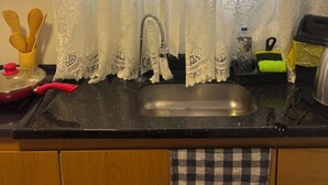 A kitchen with a sink, a faucet, a red pot, and a checkered towel hanging on the cabinet door.