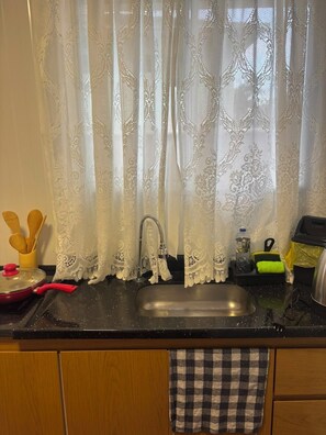 A kitchen with a sink, a faucet, a red pot, and a checkered towel hanging on the cabinet door. - New studio apartment with air conditioning, Wi-Fi, and parking. (Joinville)