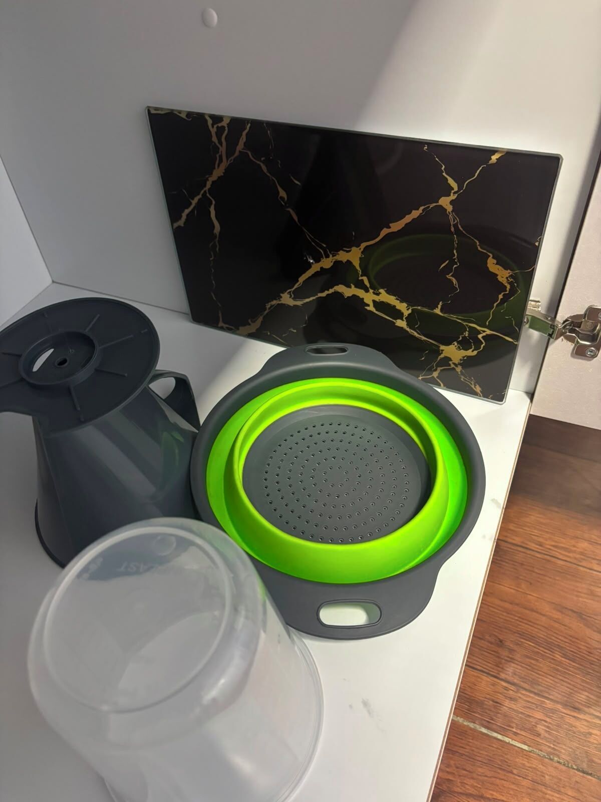 A kitchen counter with a coffee maker, a green strainer, and a clear glass.