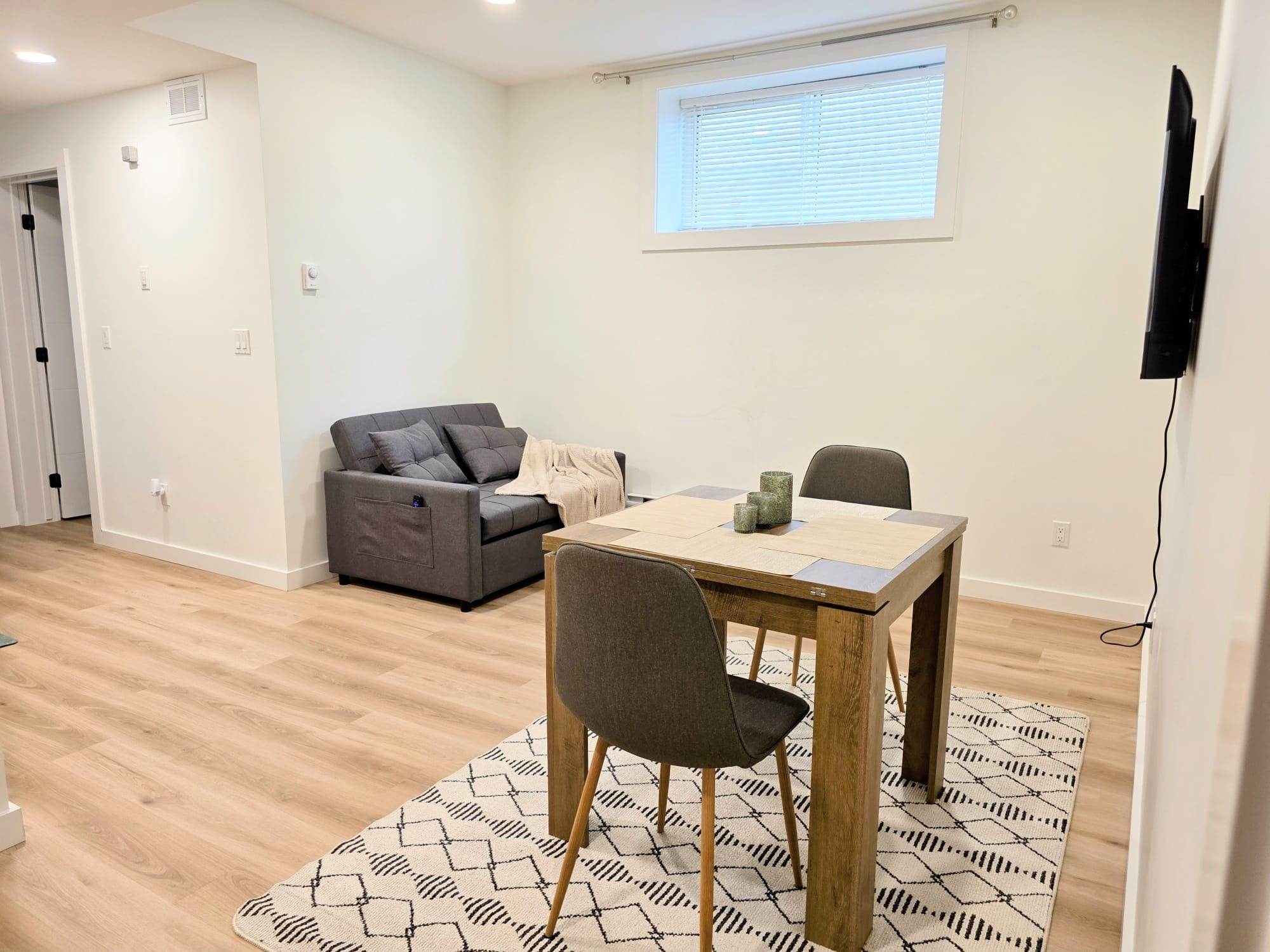 A modern living room with a sofa, a dining table, and a TV mounted on the wall.