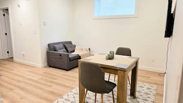 A modern living room with a sofa, a dining table, and a TV mounted on the wall.