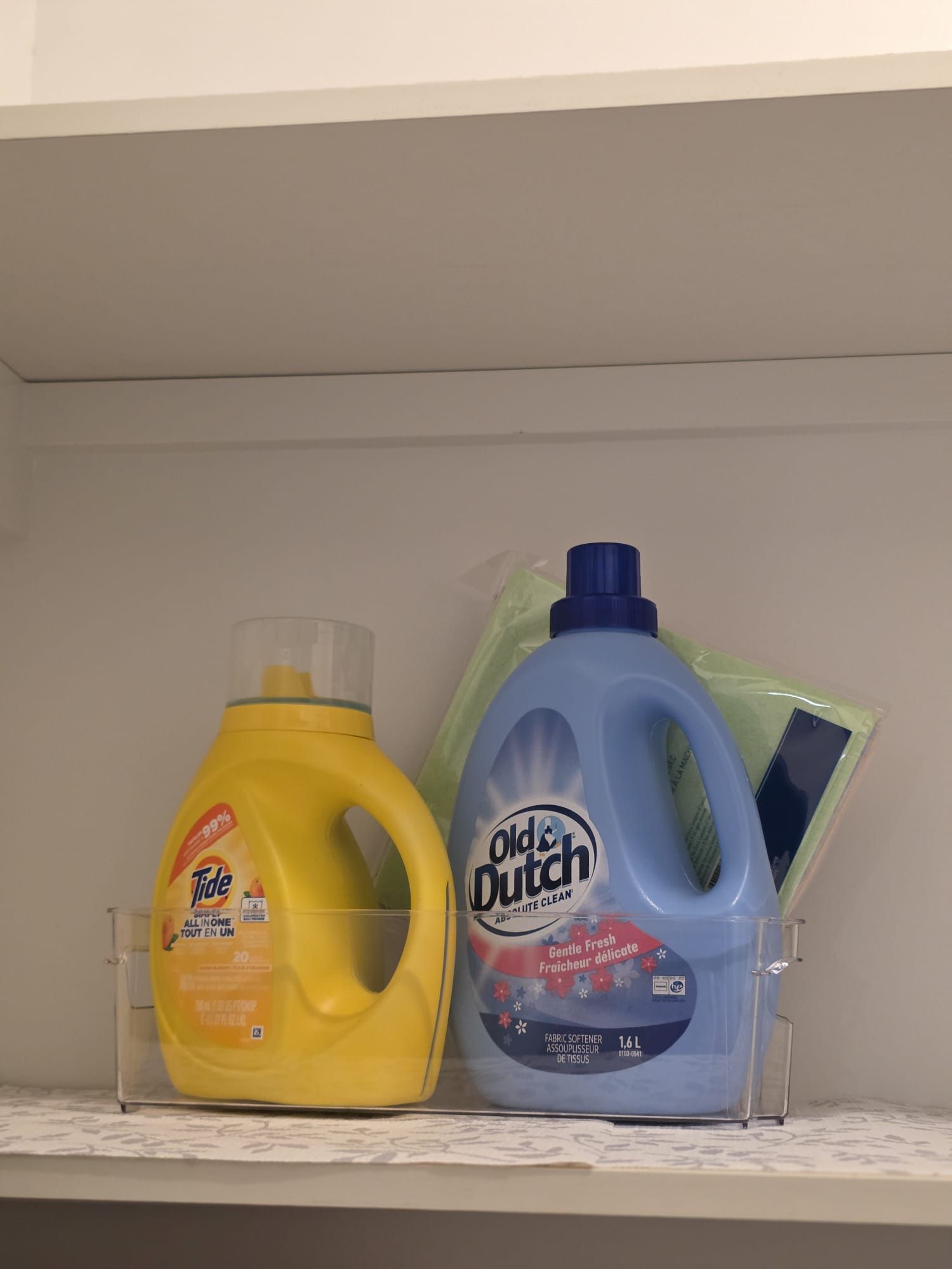 Ein Regal mit zwei Flaschen Waschmittel, eine gelb und eine blau, und einer grünen Plastiktüte.