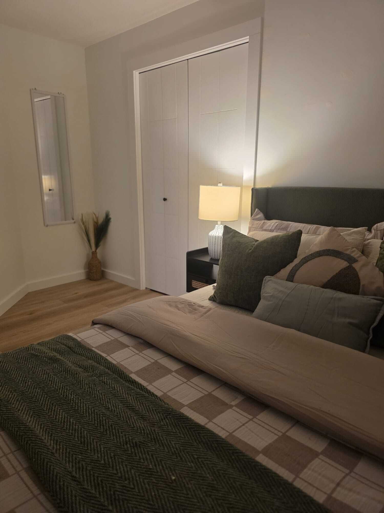 Un dormitorio con una cama, una mesita de noche, una lámpara, un espejo y una puerta.