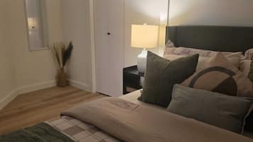 Un dormitorio con una cama, una mesita de noche, una lámpara, un espejo y una puerta.