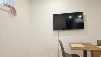 A room with a flat-screen TV mounted on the wall, a dining table with chairs, and a patterned rug on the floor.