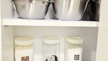 A kitchen shelf with three metal bowls and three glass jars with labels.