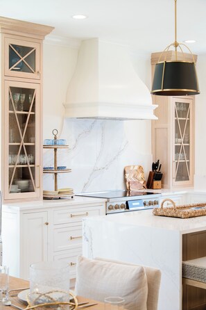 A modern kitchen with white cabinetry, a marble backsplash, and a central island with a stove. - New Beautiful Estate, Steps to Ocean, Sleeps 12 (Saco)