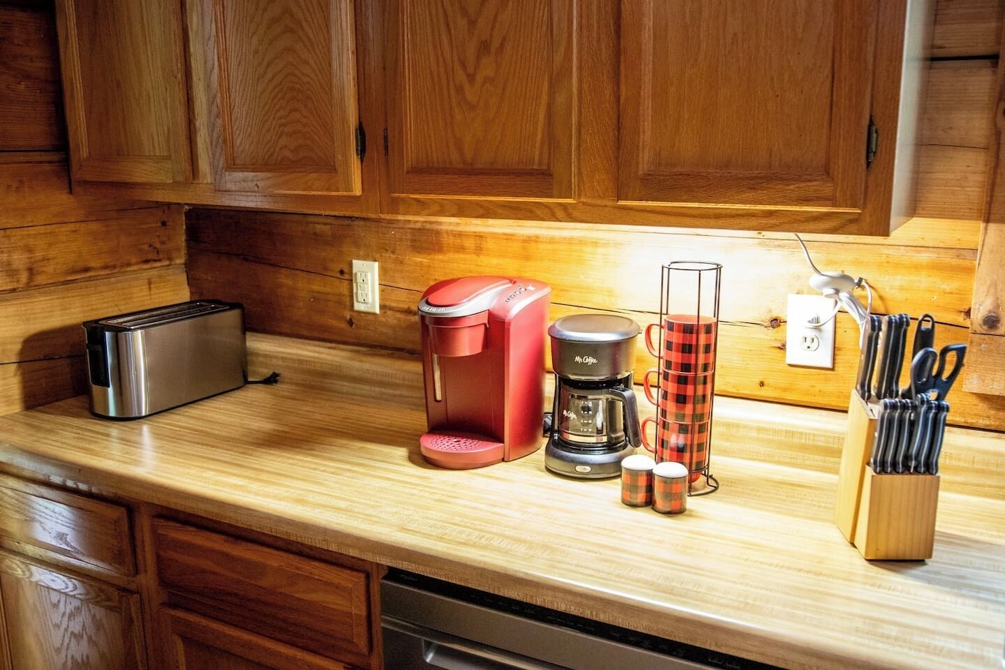 A kitchen with wooden cabinets, a toaster, a coffee maker, a mug holder, and a knife block.