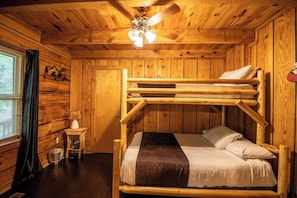 Ein Schlafraum mit Etagenbetten, Holzwänden, einem Deckenventilator und einem kleinen Nachttisch mit Lampe.