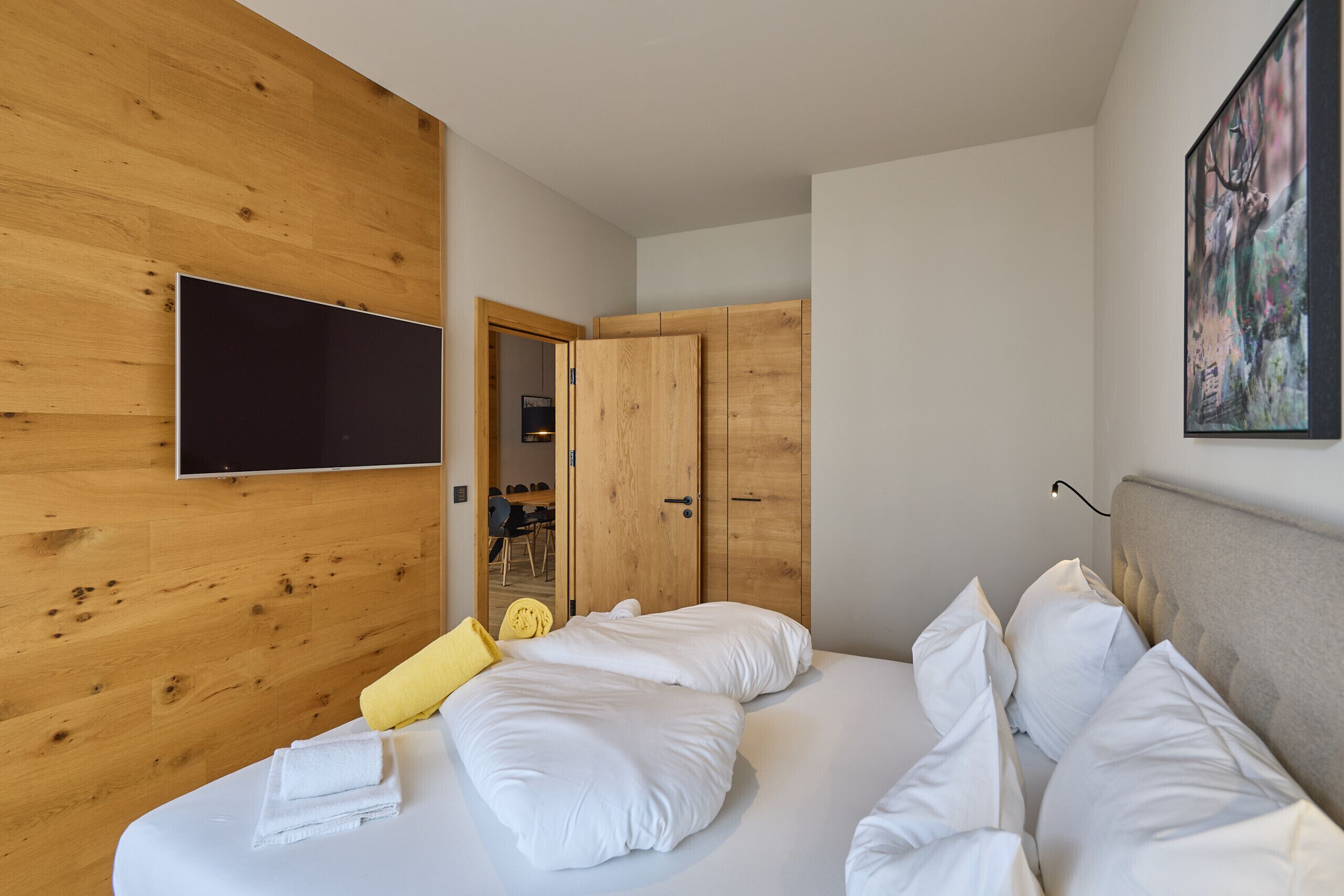 Un dormitorio moderno con una pared de madera, un televisor de pantalla plana, una cama con ropa blanca y un cuadro en la pared.