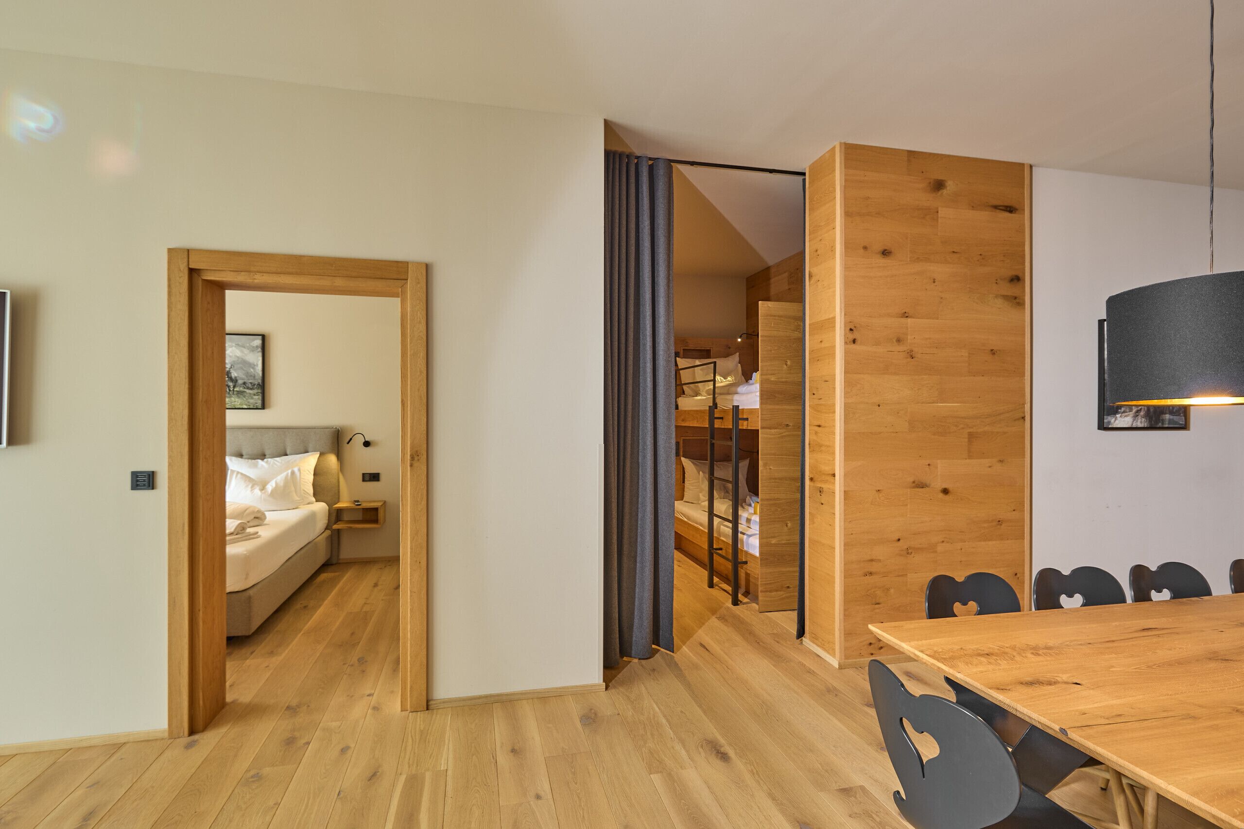 A modern hotel room with a wooden floor, a bed with white linens, a small bedside table, and a wall-mounted light fixture.
