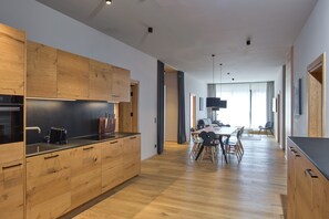 Eine moderne Küche mit Holzausstattung, ein Essbereich mit Tisch und Stühlen sowie Blick auf das Wohnzimmer.